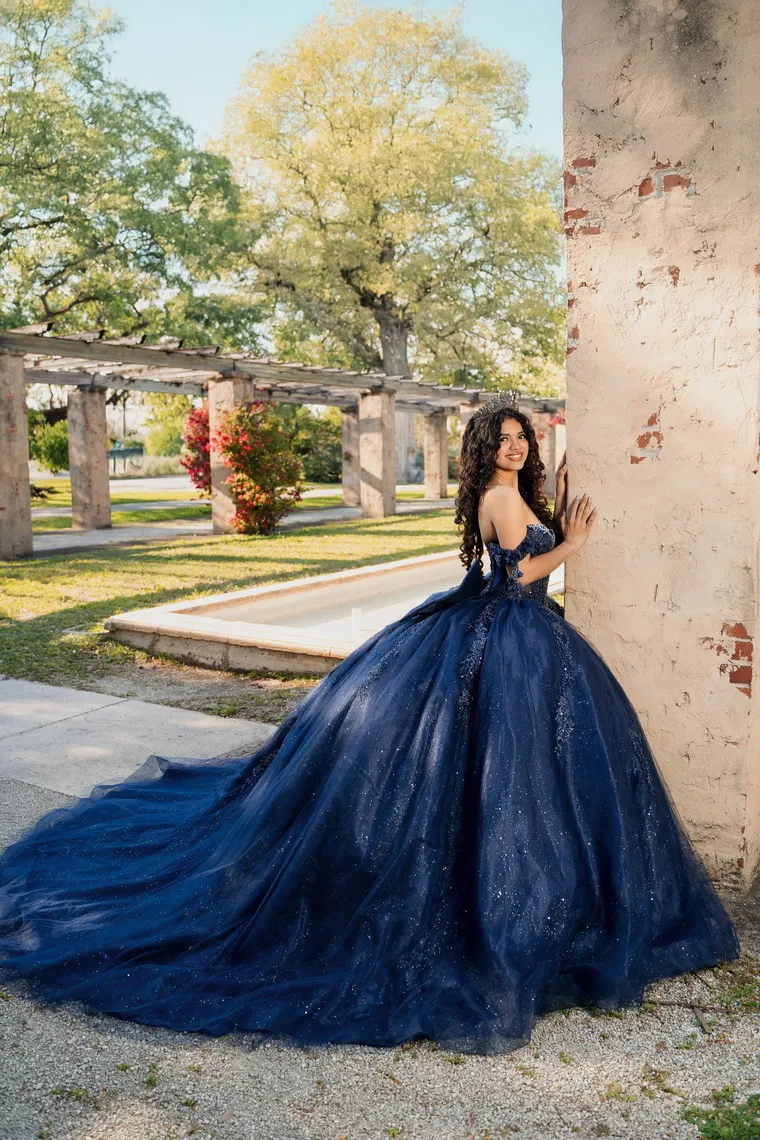 Quinceañera con vestido azul marino brillante y larga cola junto a una columna desconchada, de Photoluv Studios en Miami