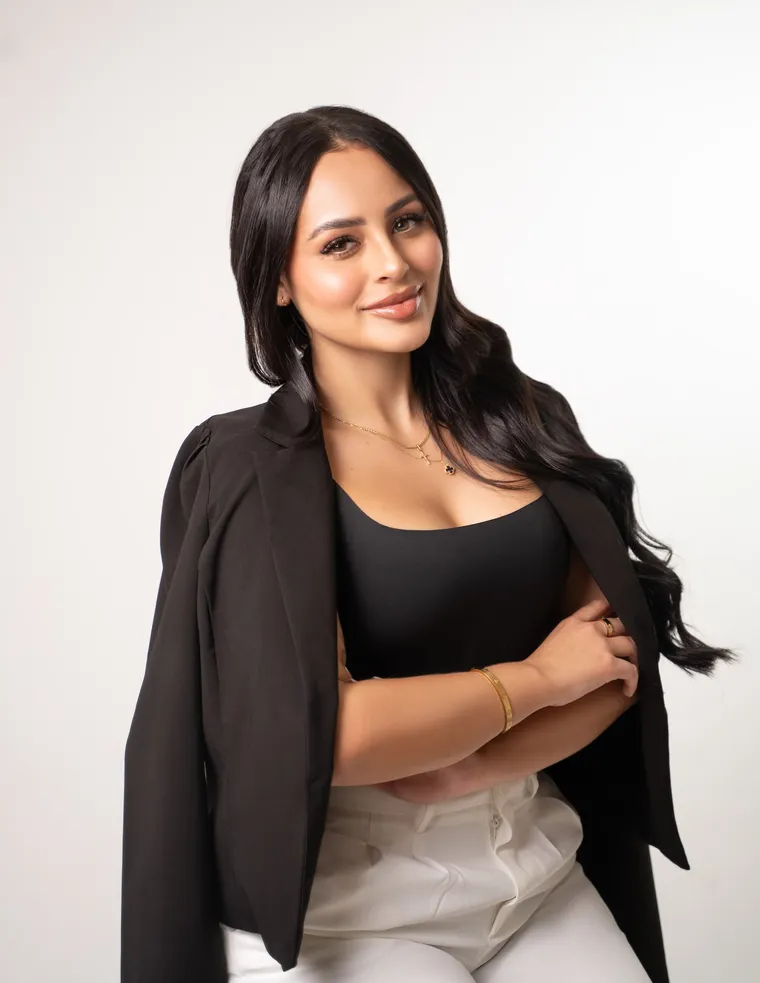 Mujer con blazer negro al hombro y pantalón blanco cruza los brazos sobre fondo blanco, de Photoluv Studios en Miami