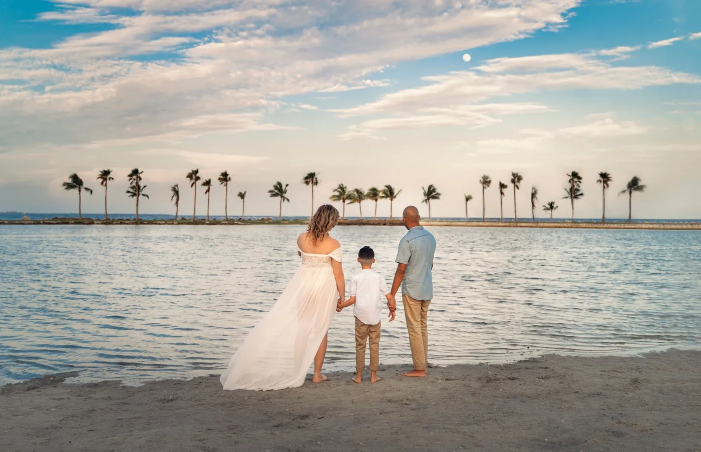 Tres personas de espaldas en la orilla, vestido blanco largo y palmeras al atardecer, de Photoluv Studios en Miami